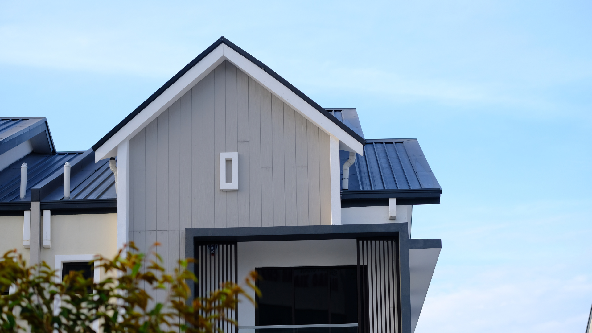 Modern gray house exterior with blue metal roof against a clear sky