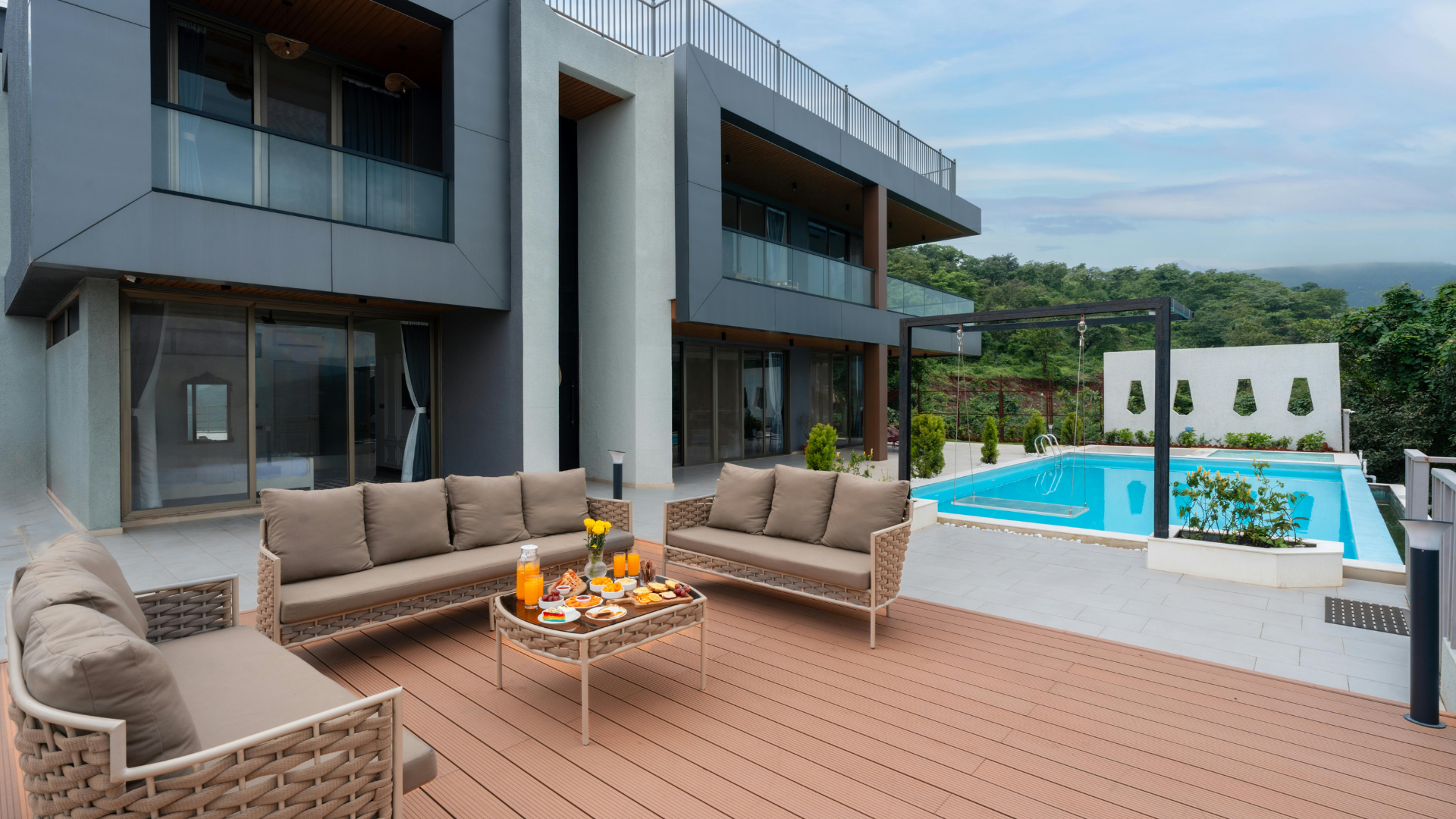 Modern patio with wicker seating, fire pit, pool, and contemporary house overlooking a lush landscape