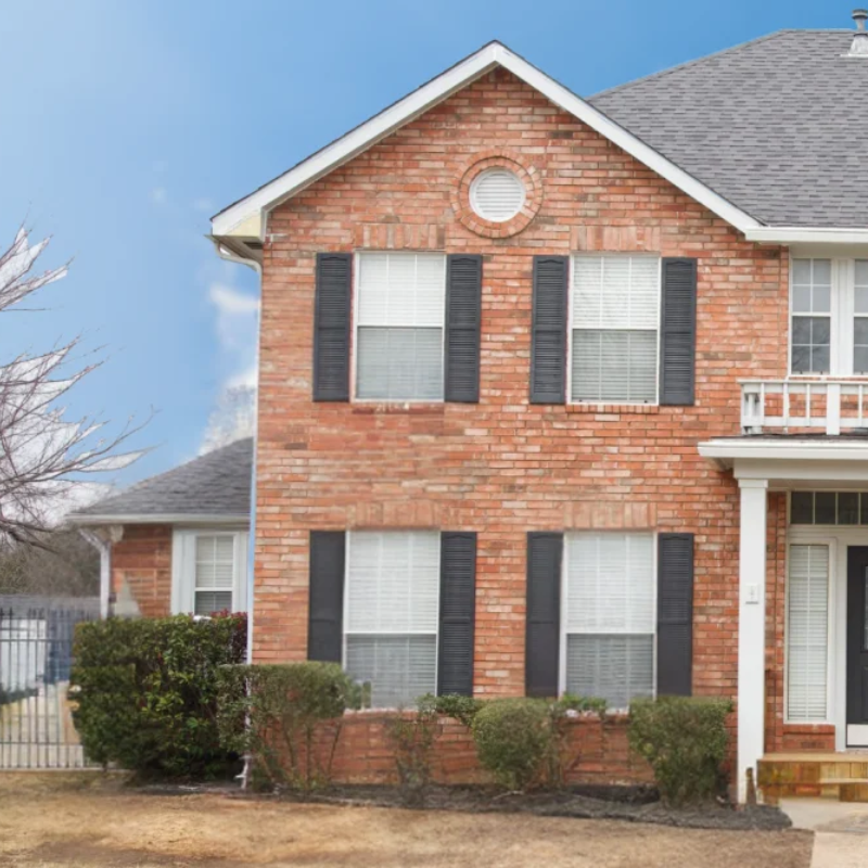 Brick two-story suburban house with black shutters and a front porch under a clear blue sky