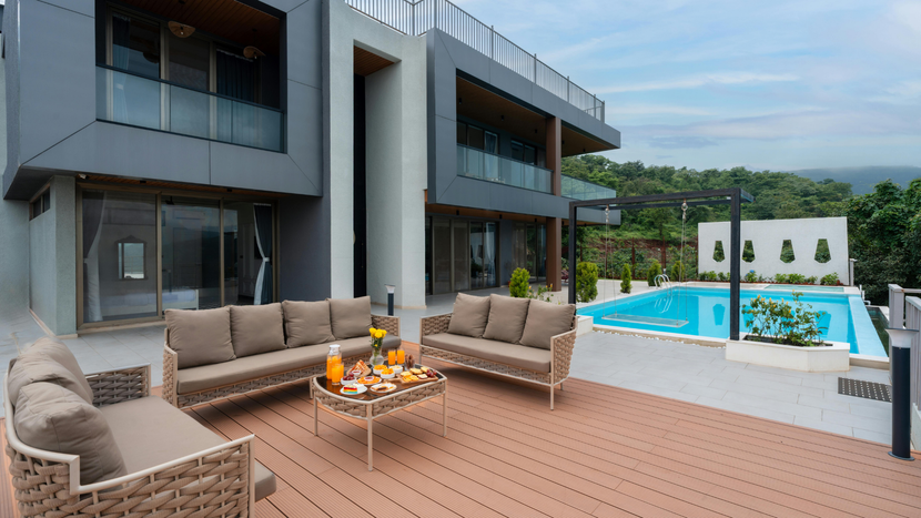 Modern patio with wicker seating, fire pit, pool, and contemporary house overlooking a lush landscape