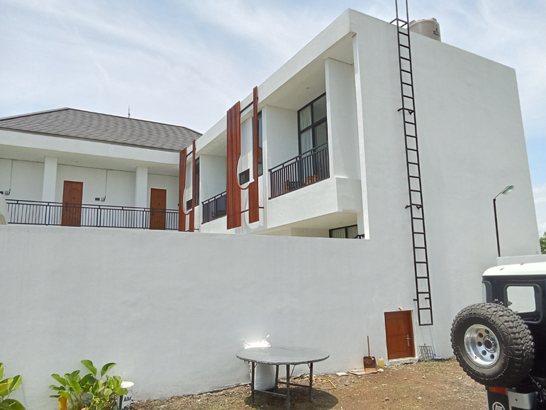 White modern house behind a high wall with a ladder, small table, and parked vehicle at right