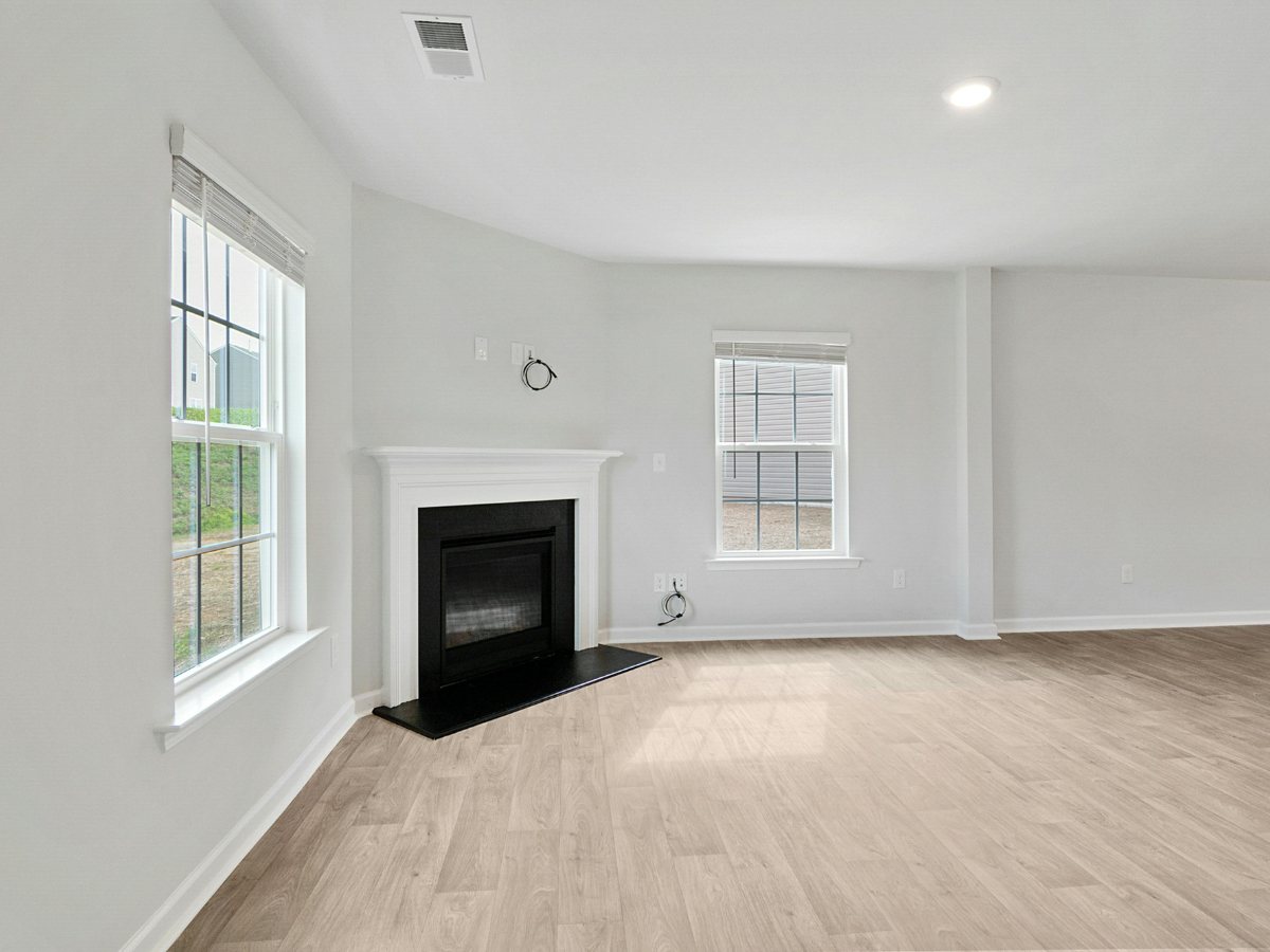 Bright empty living room with white walls, wood floors, fireplace, and large windows