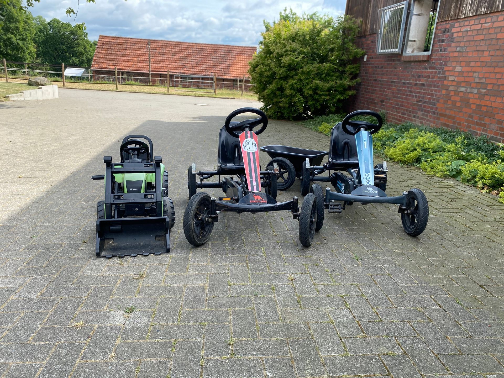Drei gokartähnliche Fahrzeuge, die auf einem Schotterweg neben einem Backsteingebäude geparkt sind