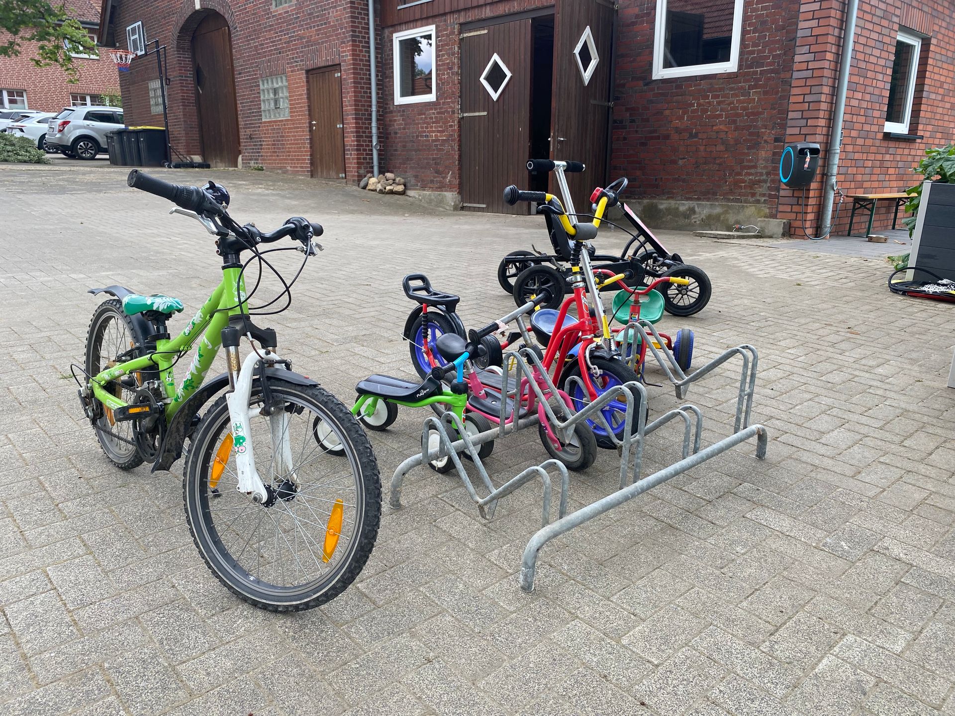 Drei farbenfrohe Kinderfahrräder stehen in einem Fahrradständer vor einem Backsteingebäude.