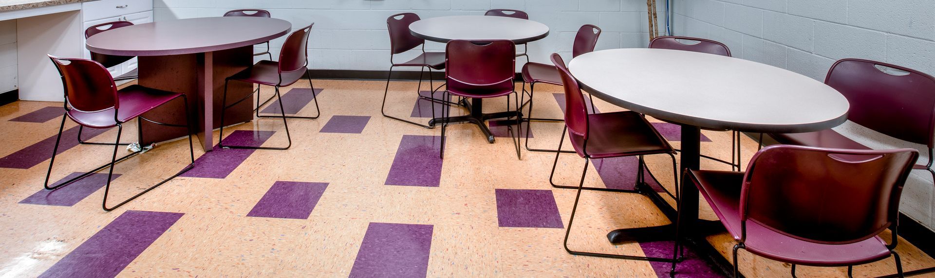 A room with multiple round tables and chairs. The floor is tiled in a purple and tan pattern.