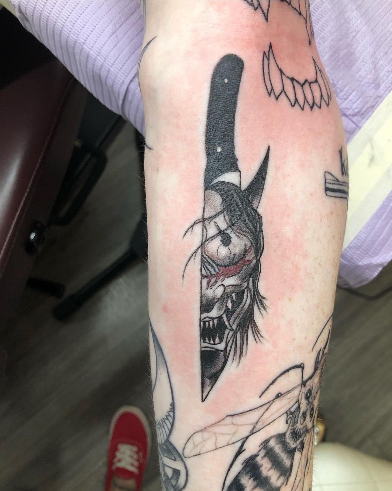 Forearm with black-and-gray tattoo featuring a masked face and dagger design