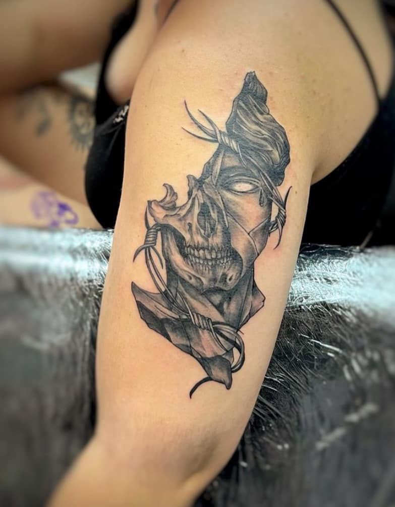 Black and gray tattoo of a hooded skull on an upper arm, shown close-up.