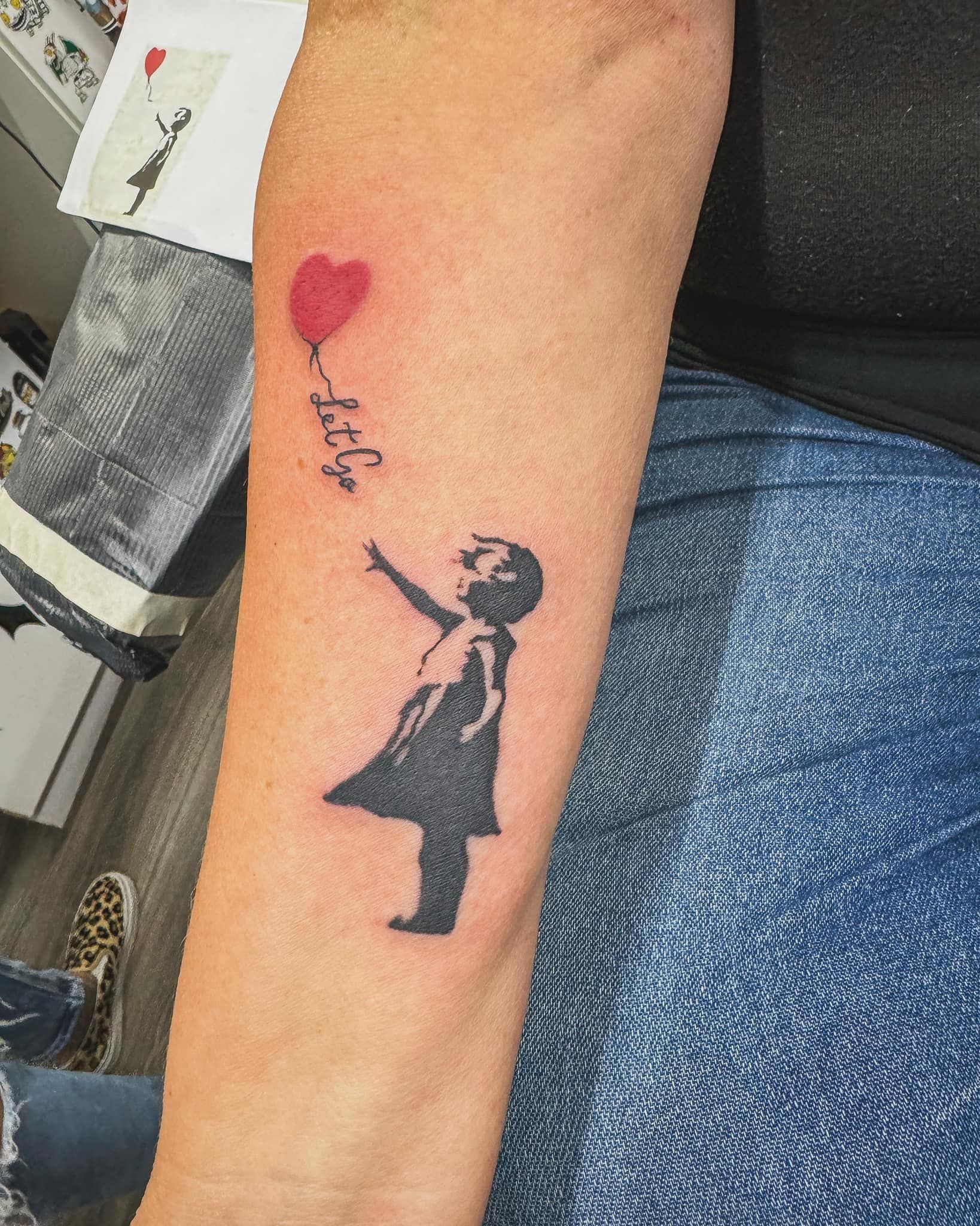 Forearm tattoo of a girl reaching for a red heart, with the word “love” above it.