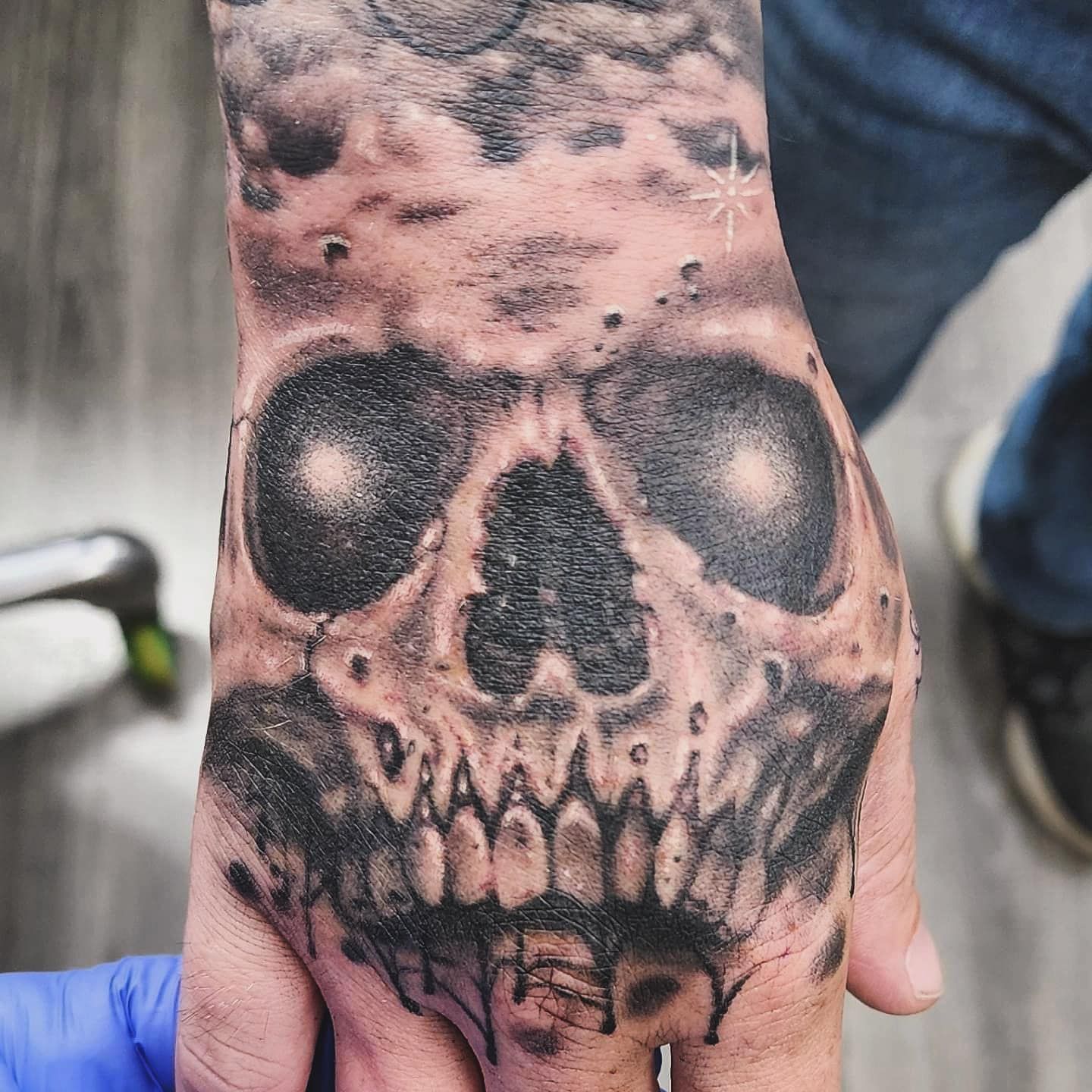 Close-up of a hand with a black skull tattoo on the back of the wrist.