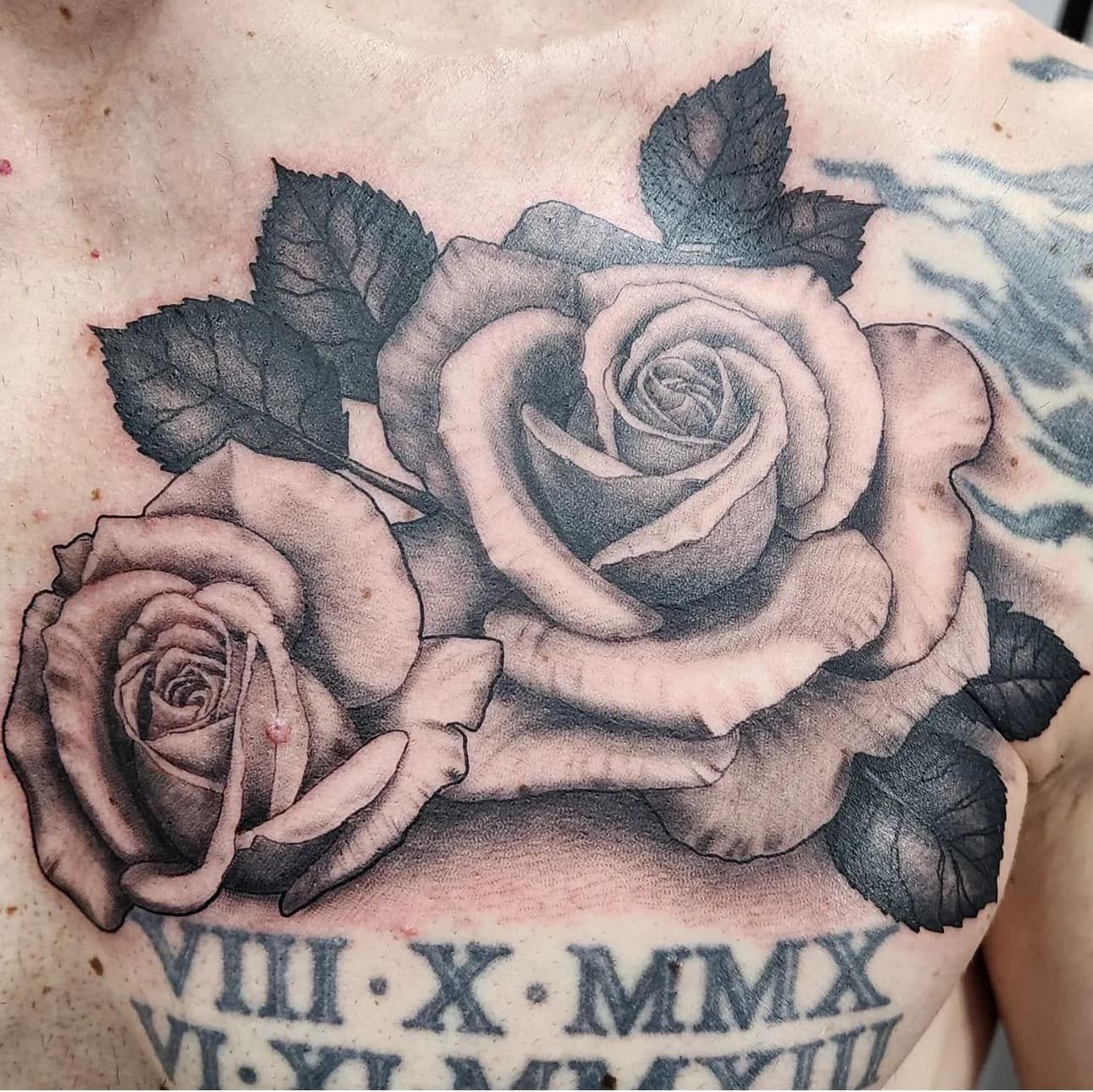 Close-up of a rose tattoo with Roman numerals on skin, in black and gray ink