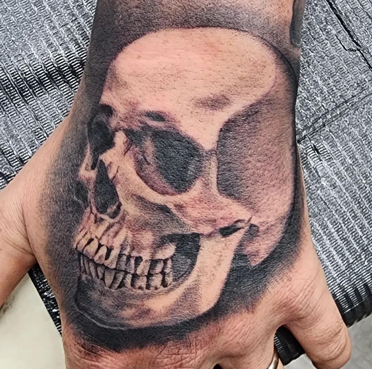 Hand tattoo of a realistic skull with dark shading on the back of a hand