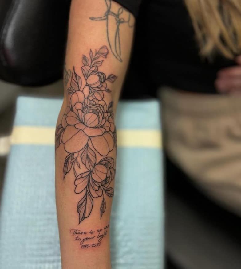 Floral tattoo on a forearm with outlined flowers and leaves, plus small text near the wrist