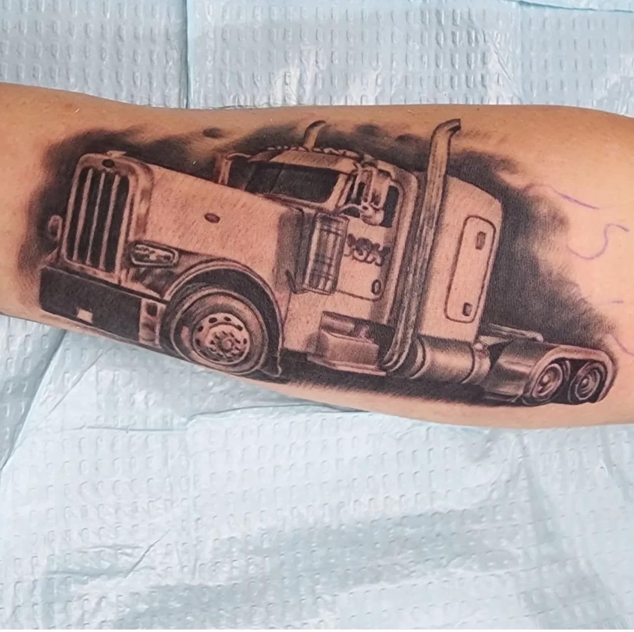 Black and gray tattoo of a semi-truck on an arm, with shading and a vintage look