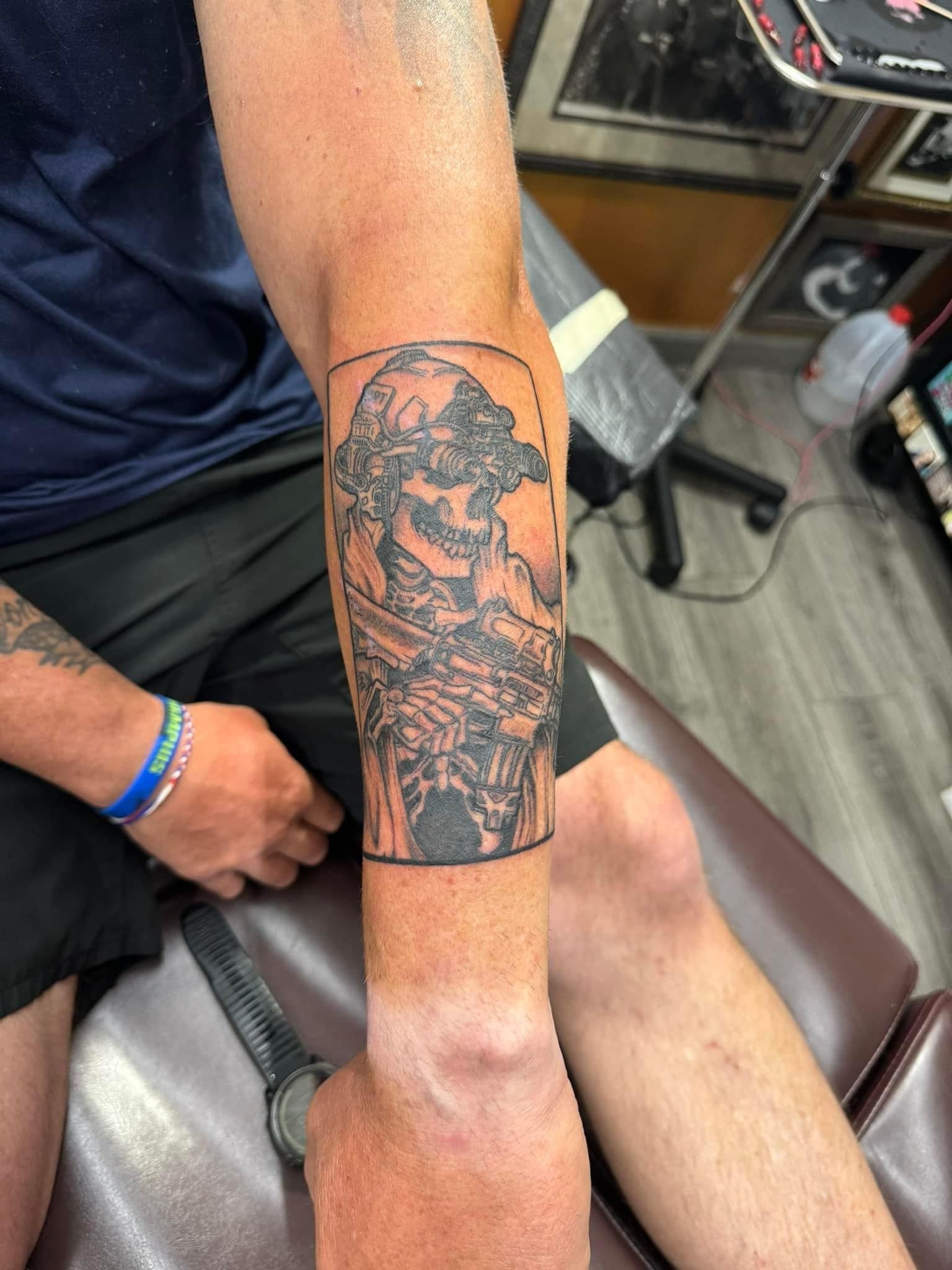 Arm resting on chair, showing a dark forearm tattoo in a tattoo shop setting.