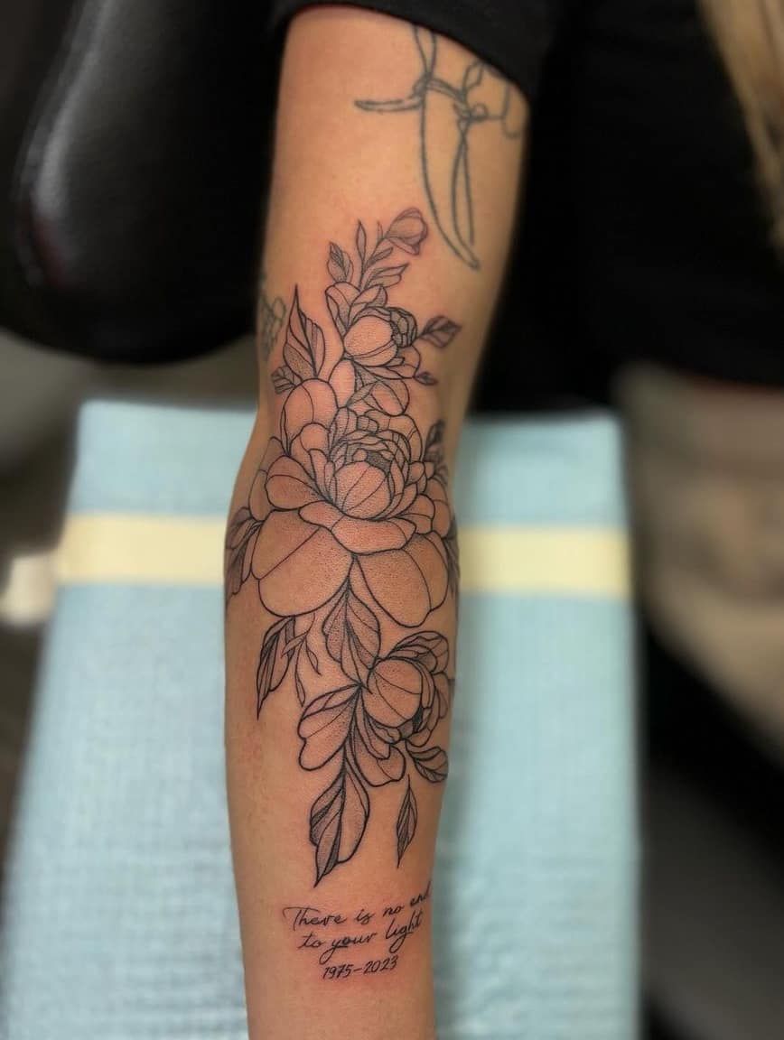 Close-up of a floral line-art tattoo on a forearm, with a small handwritten quote near the wrist.