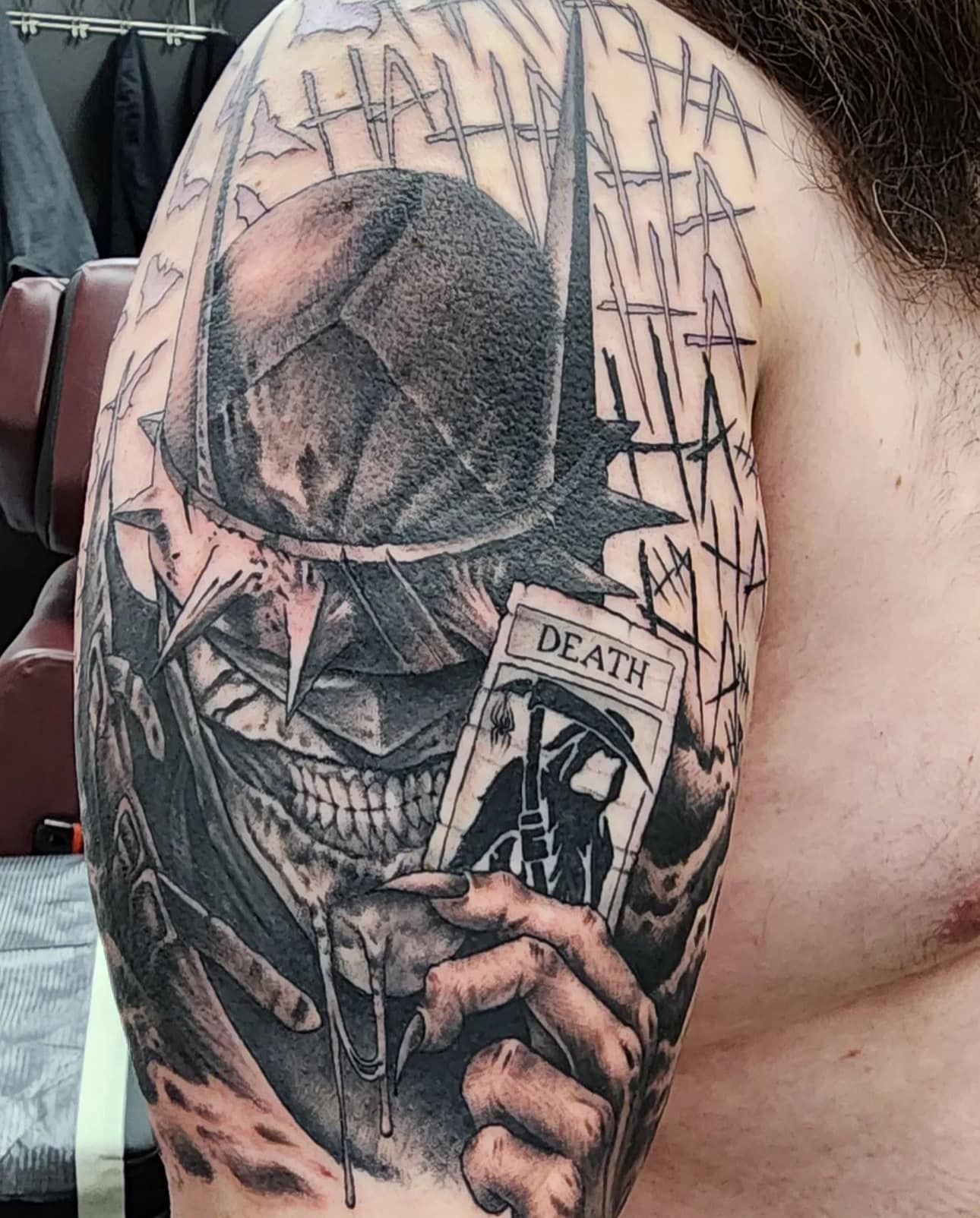 Close-up of a black-and-gray skull tattoo wearing a hat, holding a “Death” card on a cheek
