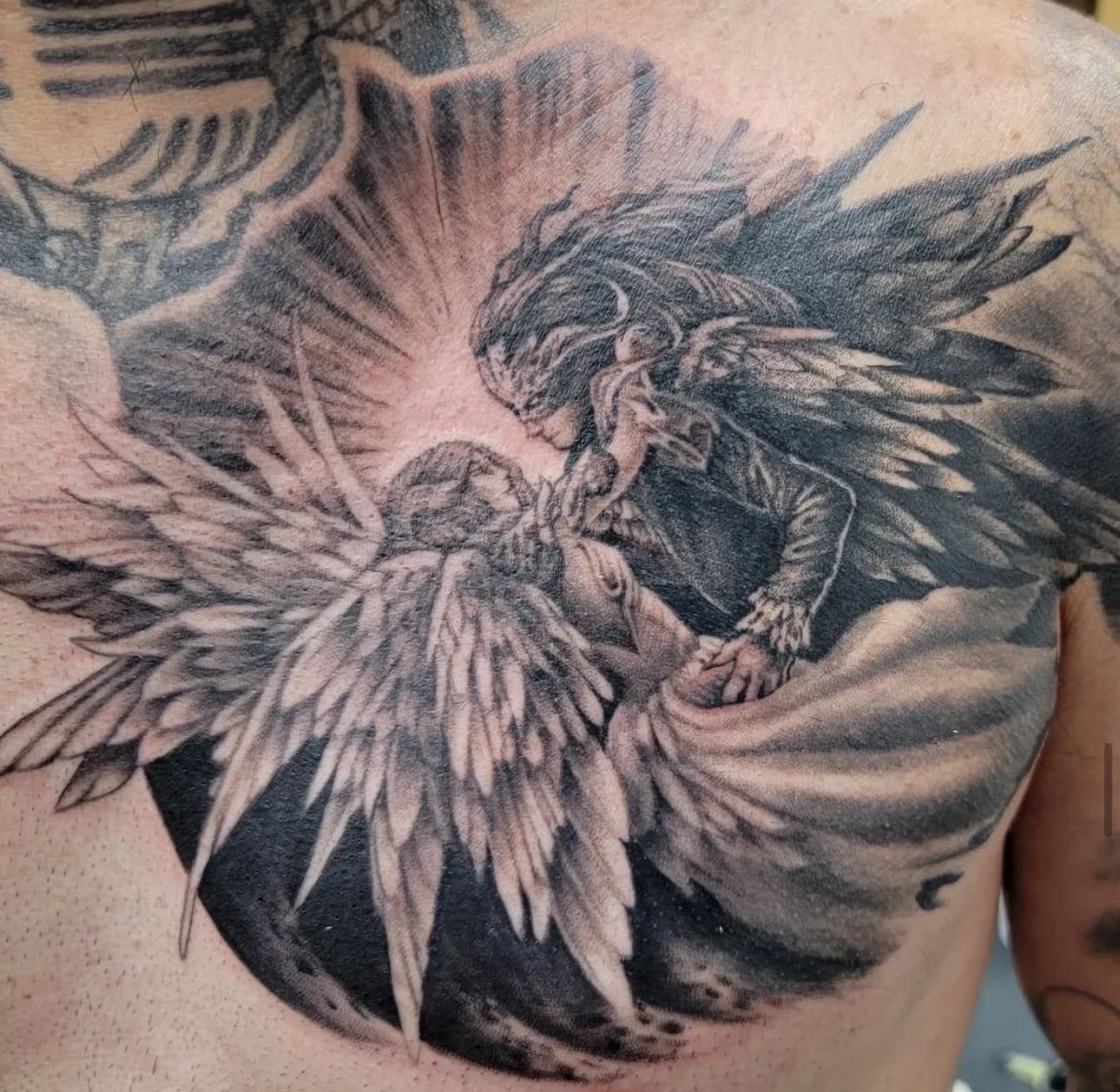 Black-and-gray angel tattoo with spread wings on a person’s upper back