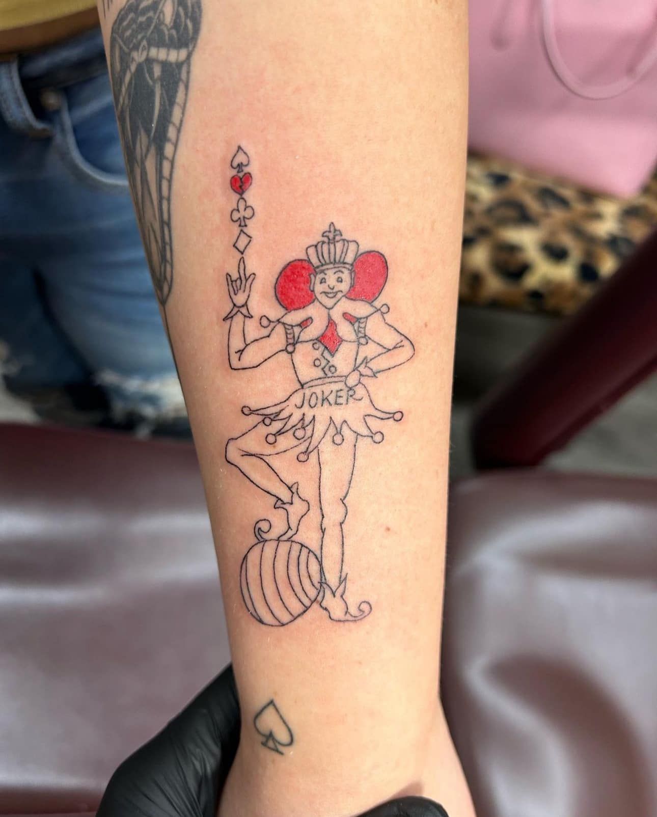 Forearm tattoo of a colorful playing-card joker with staff and striped pants