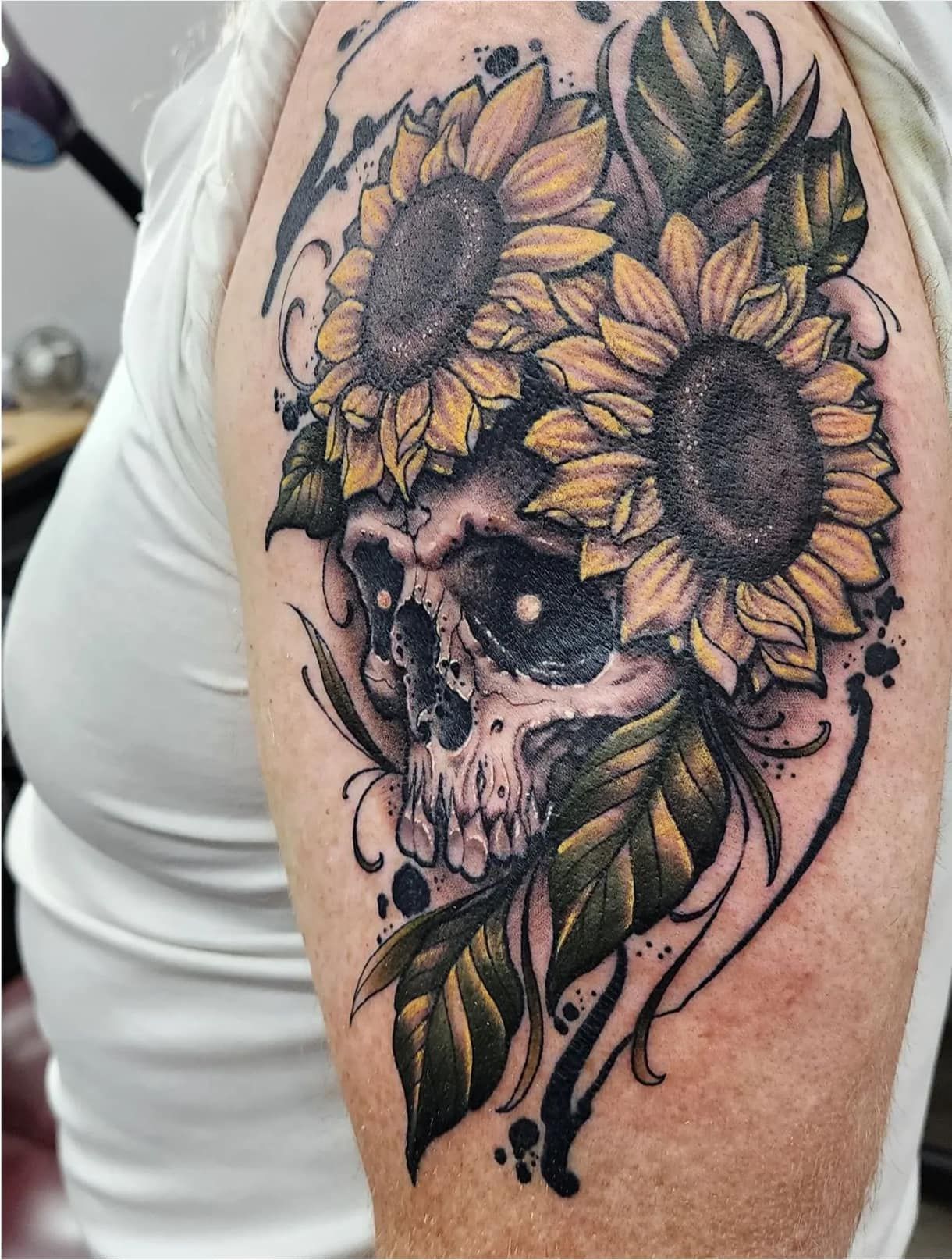 Sunflower and skull tattoo with black-and-gray shading on an upper arm