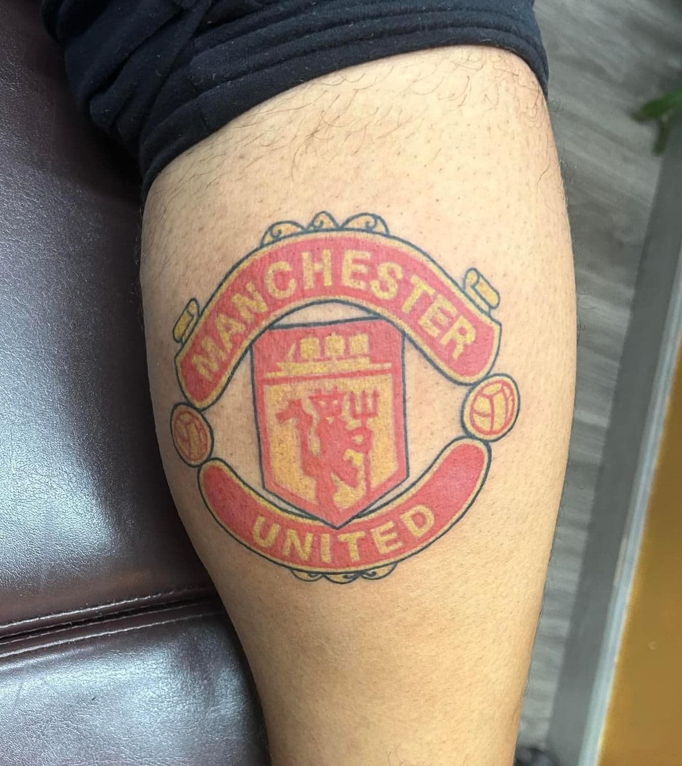 Close-up of a leg with a Manchester United crest tattoo in red and gold