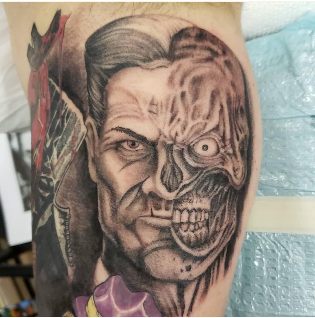 Close-up of a black-and-gray tattoo of a half-human, half-skeletal face on an arm