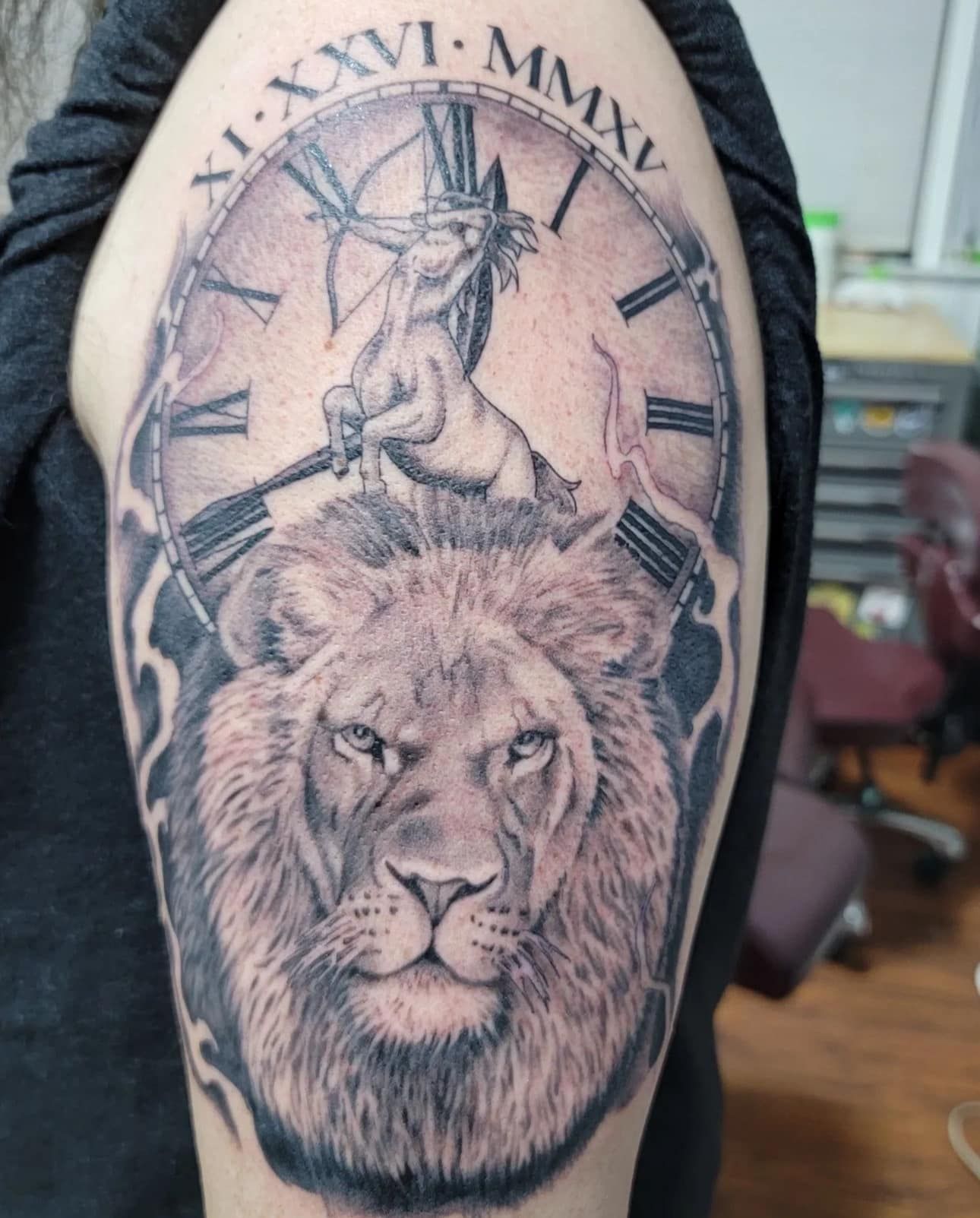Black-and-gray tattoo of a lion’s face with a unicorn above and Roman numerals around it on a forearm