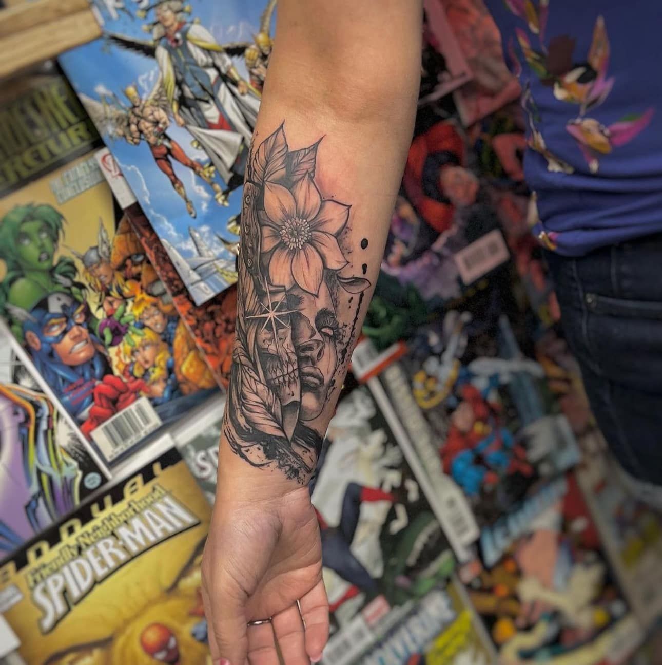 Arm with black floral tattoo in front of a colorful comic book display