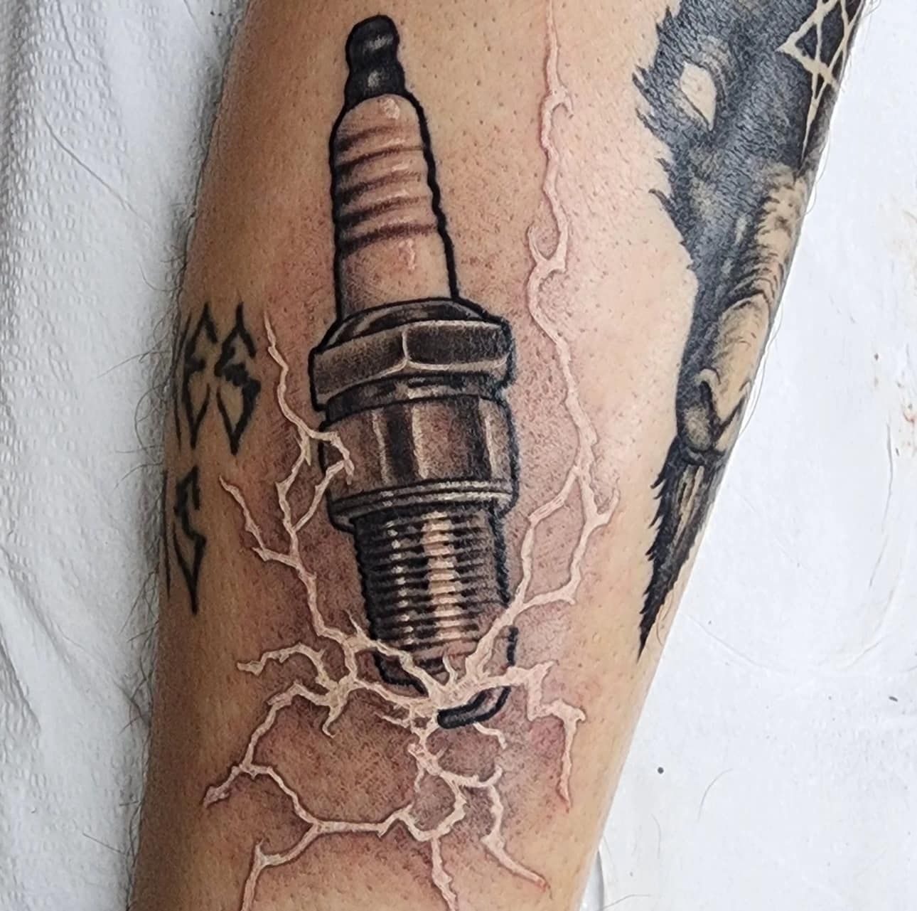 Tattoo of a spark plug with lightning cracks on a forearm, black and pink ink