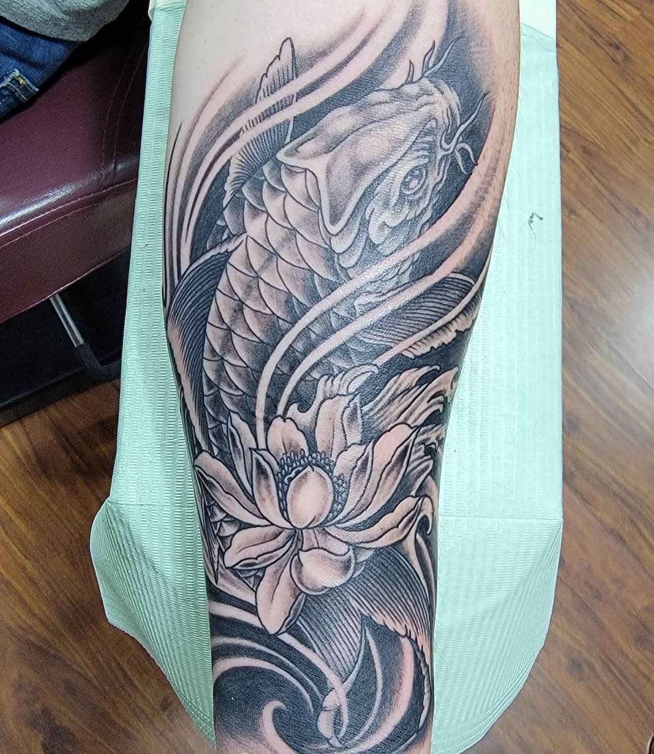 Black-and-gray floral tattoo on a leg, featuring a koi fish and flowing waves.