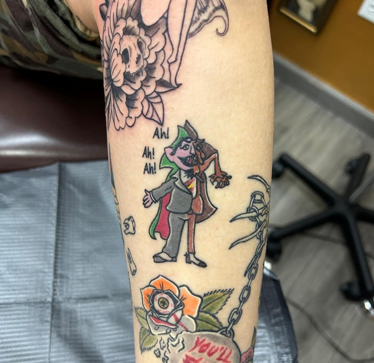 Forearm with colorful tattoos, including a small green-and-purple character and floral designs