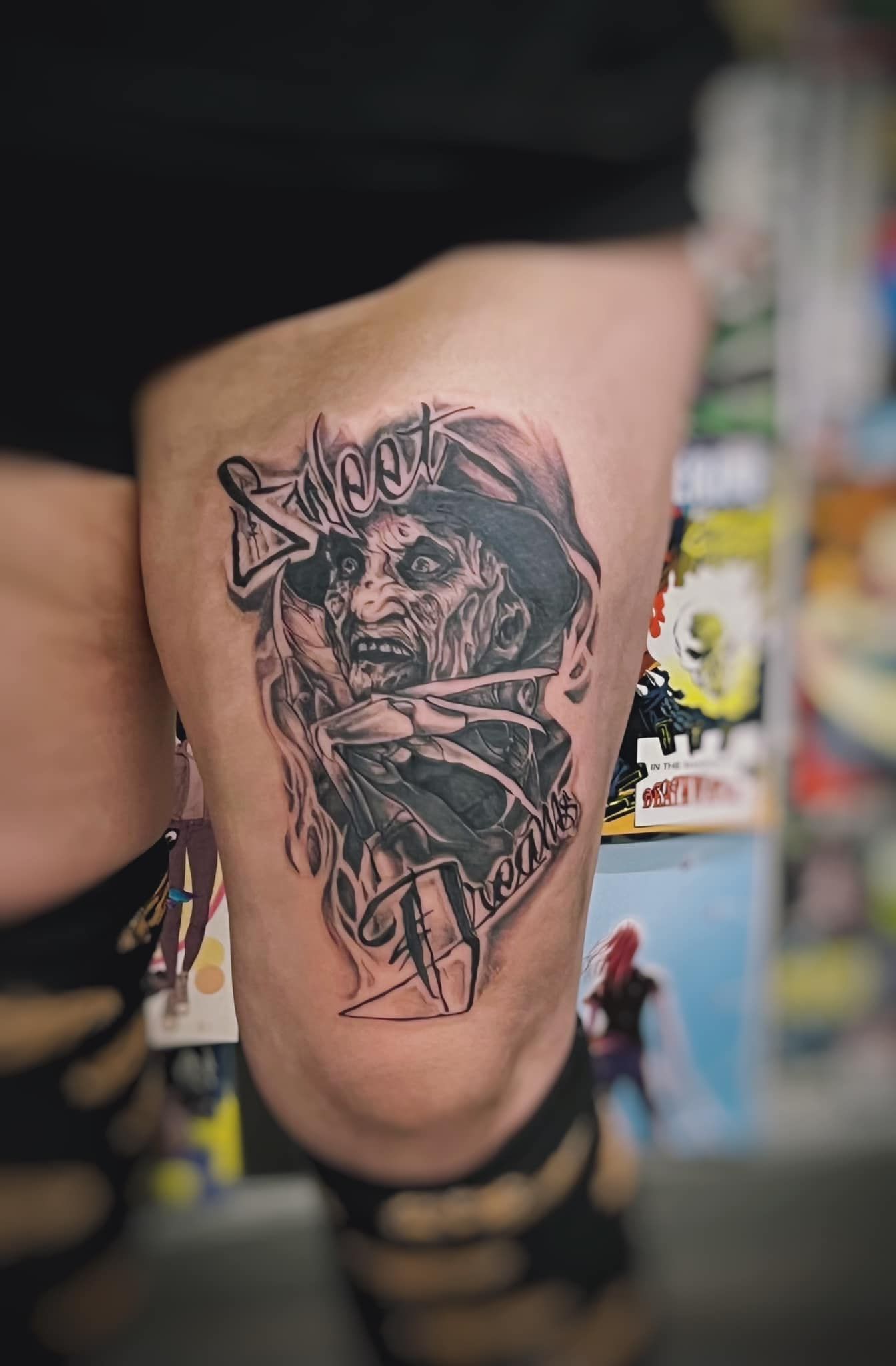 Close-up of a colorful tattoo on a lower leg, showing a detailed portrait with bold black outlines.