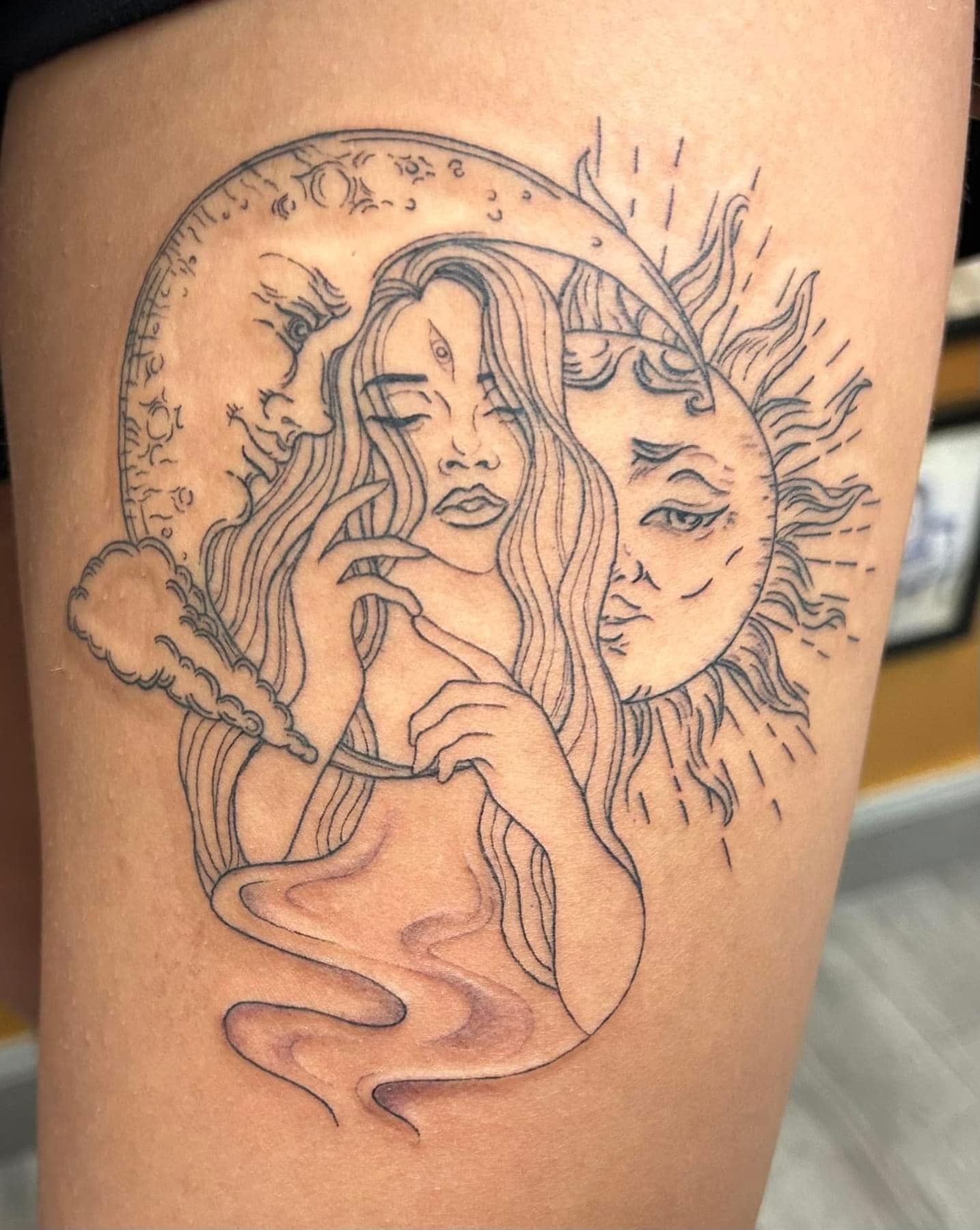 Black line-art tattoo of three stylized faces with flowing hair and abstract shapes on skin
