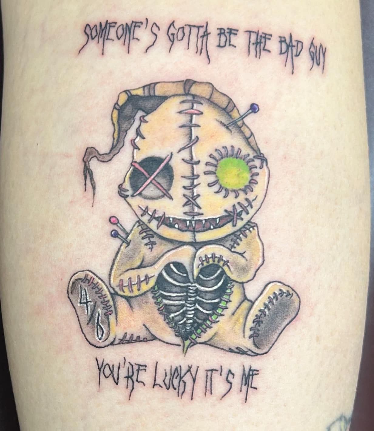 Stitched rag doll tattoo with crooked eyes and sun emblem, with handwritten text above and below.