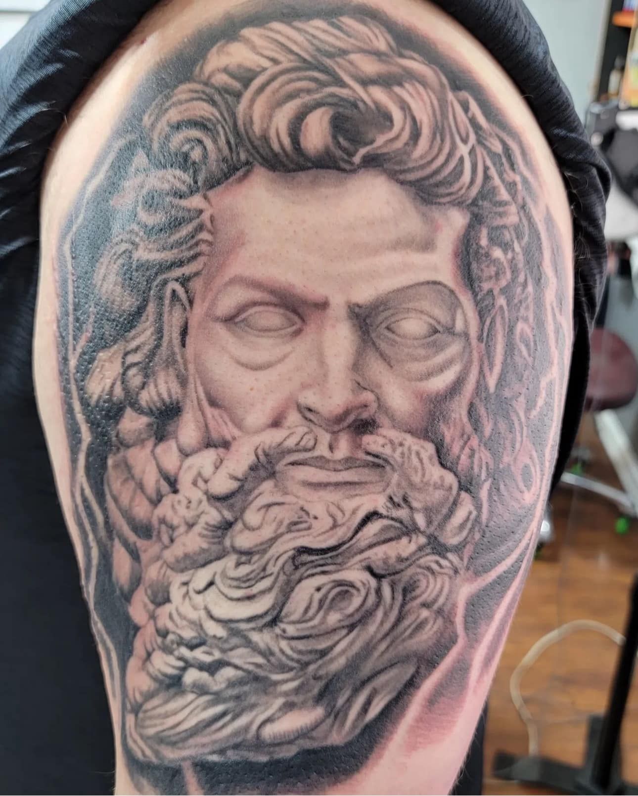 Black-and-gray tattoo of a classical bearded face with closed eyes on a person’s shoulder