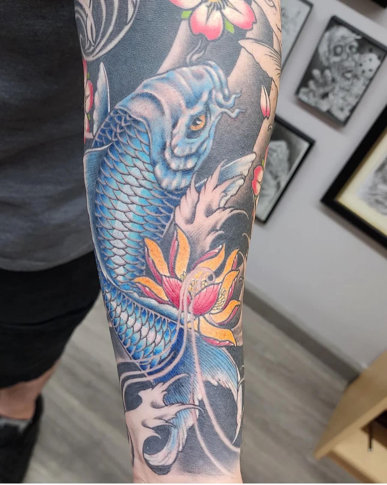 Colorful blue koi fish tattoo with pink lotus flowers on a forearm