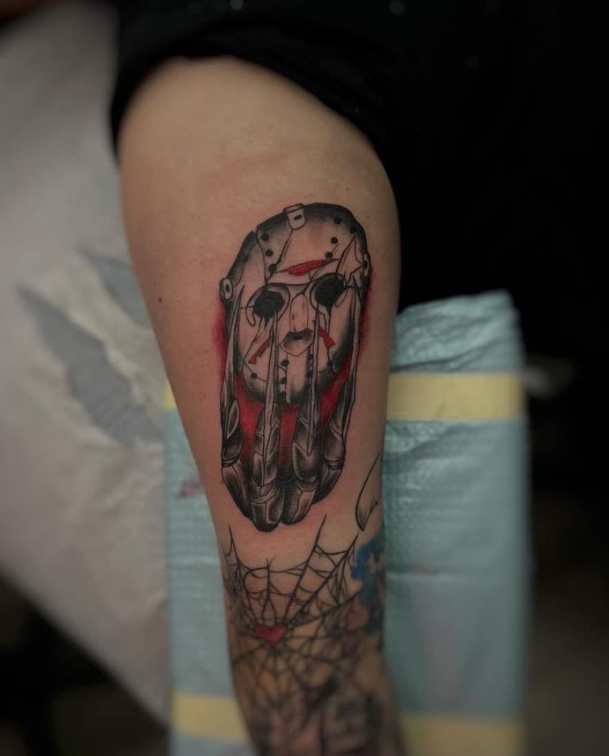 Close-up of a forearm tattoo showing a grim face with dark red and black details.
