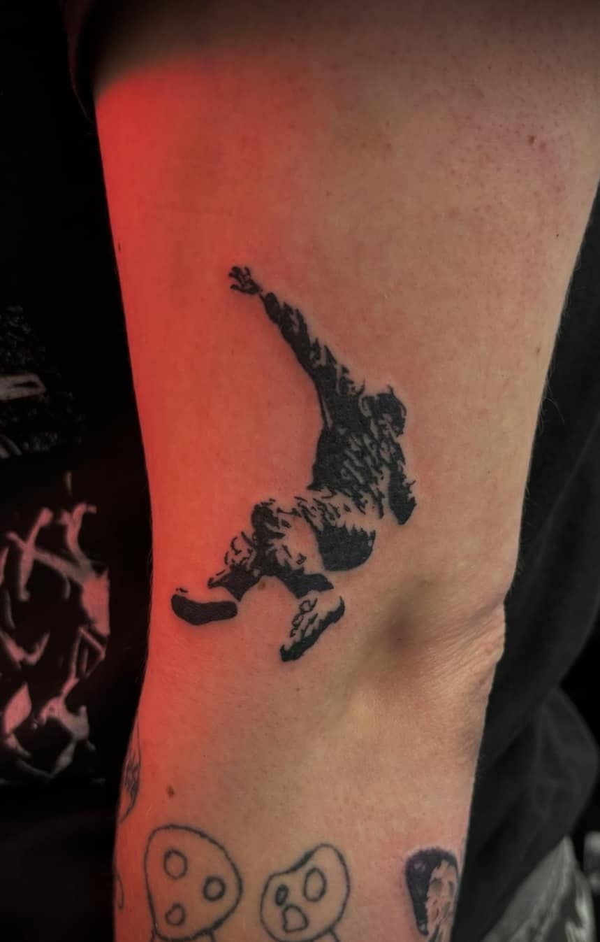 Close-up of a forearm with a black tattoo of a person jumping, lit by red light.
