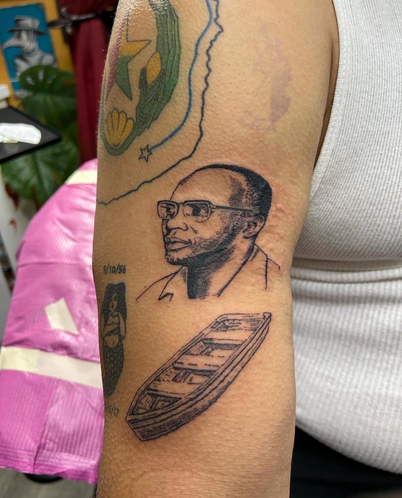Close-up of an arm with black line-art tattoos, including a portrait and a canoe-like design.