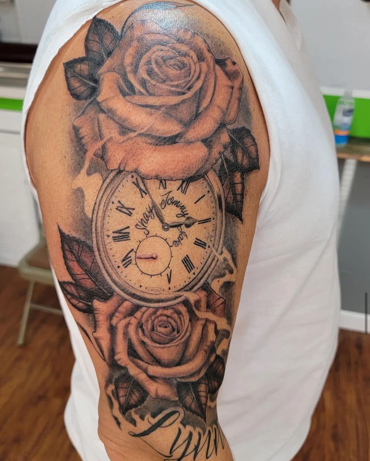 Arm tattoo featuring a rose, compass, and skull in black and gray ink