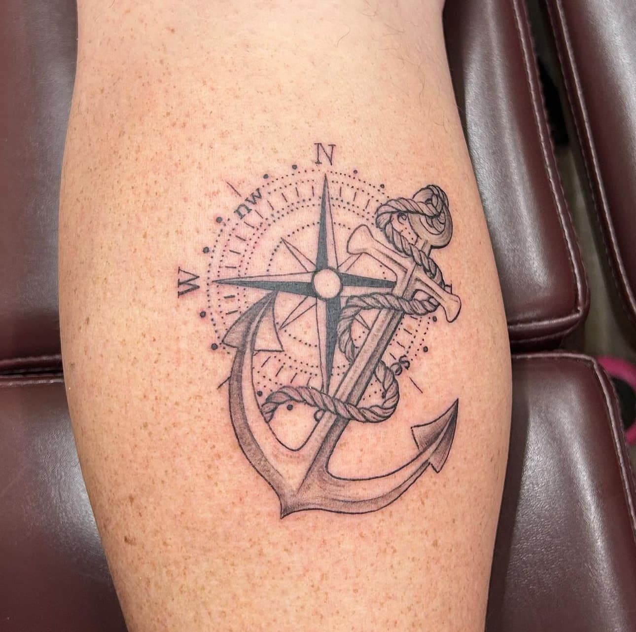 Compass and anchor tattoo on a calf, in black ink on skin.