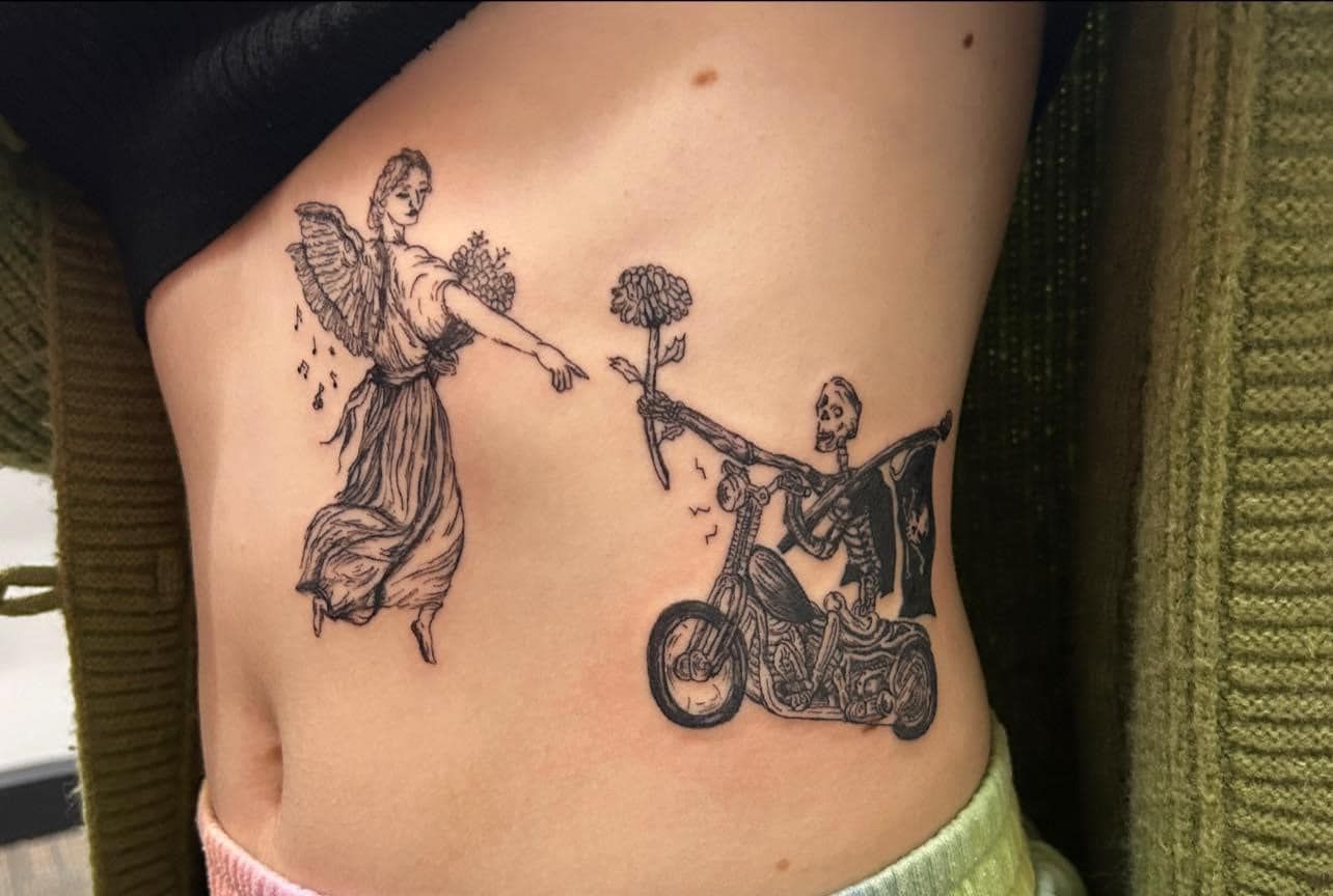 Close-up of a black line-art tattoo on skin showing a robed figure offering flowers to a person in a wheelchair