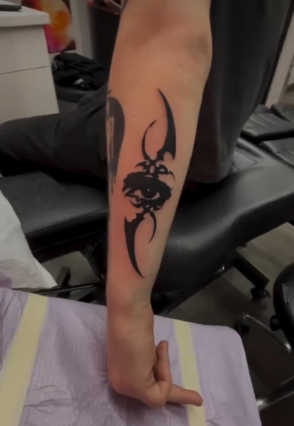 Forearm with black tribal-style tattoo on a person resting a hand on a bench in a gym.