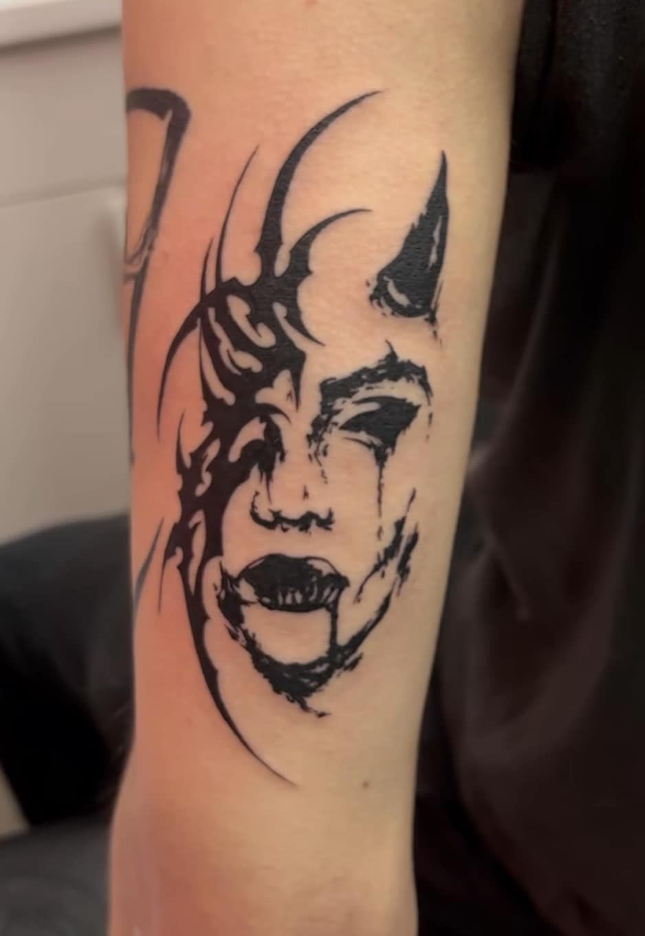 Black-and-white abstract face tattoo on a forearm, with bold black lines and dark lips.