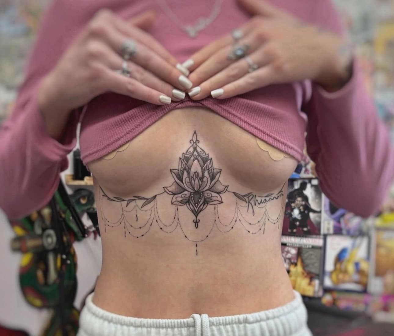 Torso with a floral sternum tattoo, hands lifting a mauve top to show it.