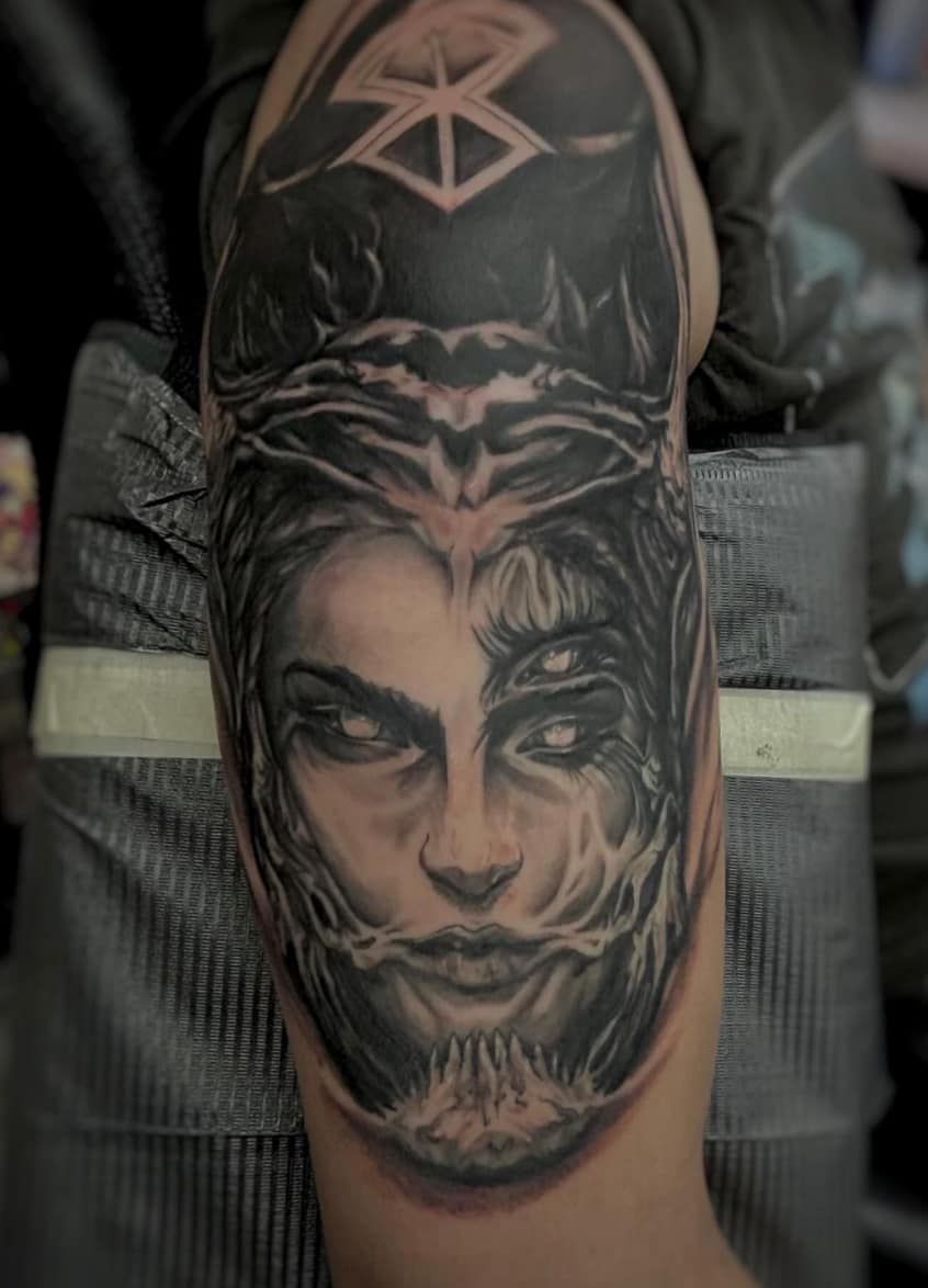 Forearm tattoo of a monochrome face with flowing hair and a star-like symbol above it