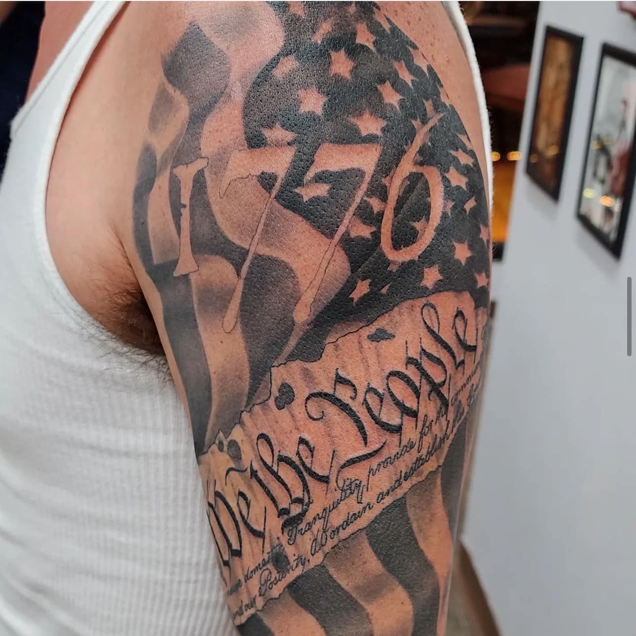 Close-up of a tattooed upper arm with black and gray script and abstract designs