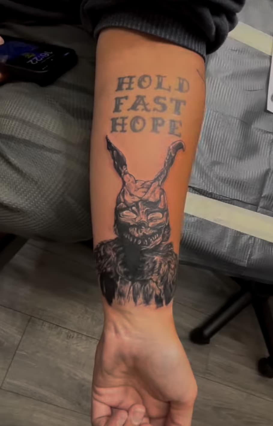 Forearm tattoo of a rabbit holding up a banner reading “HOLD FAST HOPE”