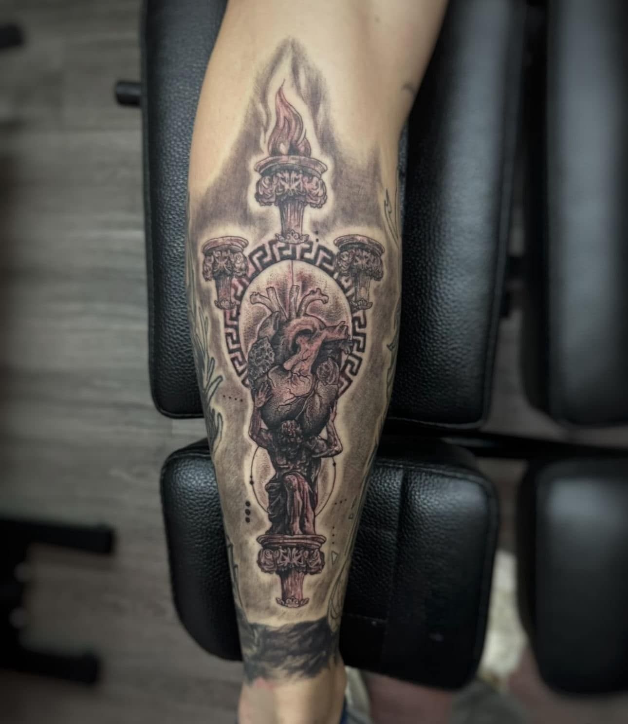 Black-and-gray tattoo of an ornate dagger and skull on a person’s forearm, resting on a chair.