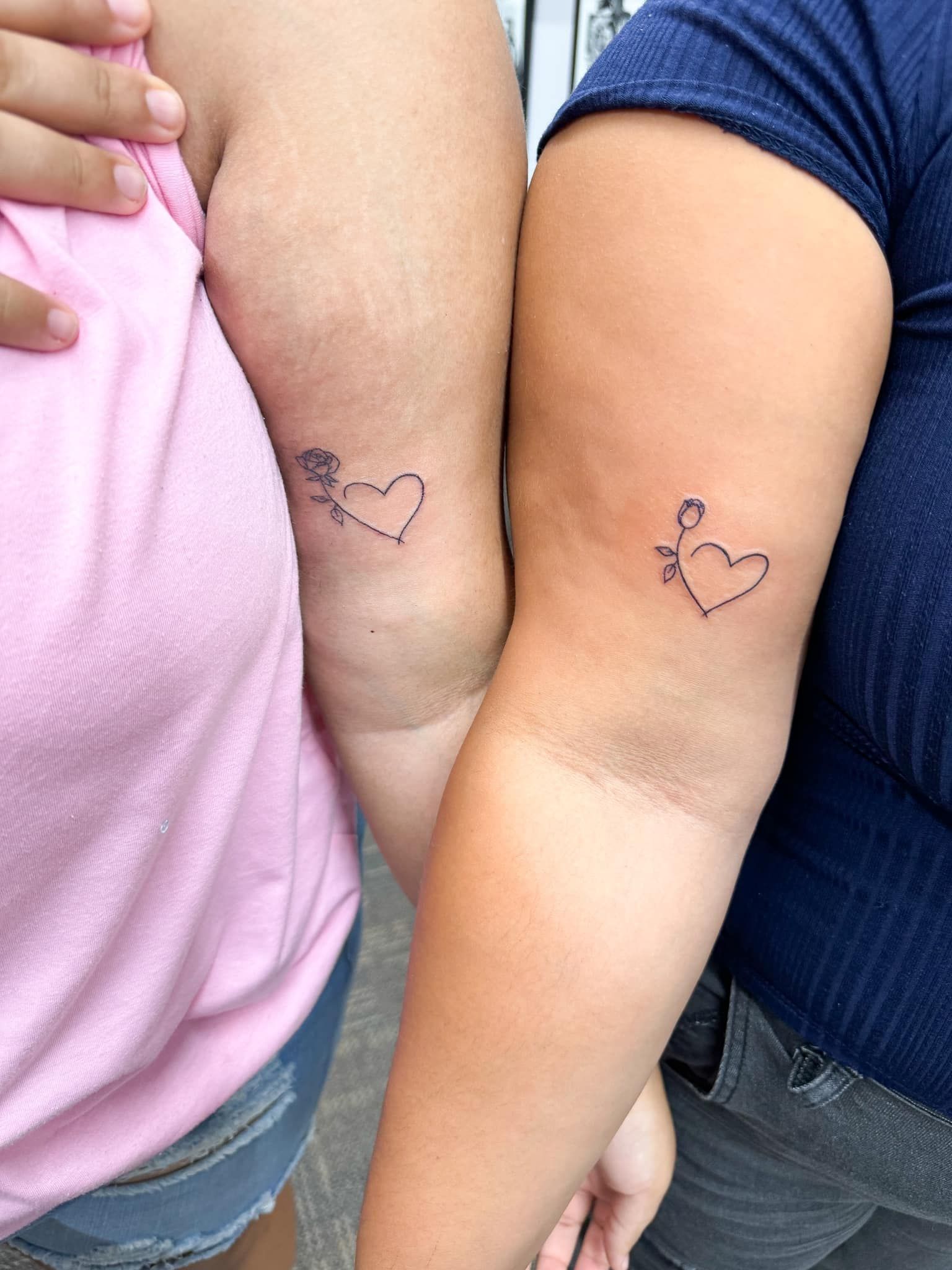 Two arms with matching heart tattoos near the elbows, one in pink and one in blue shirts.
