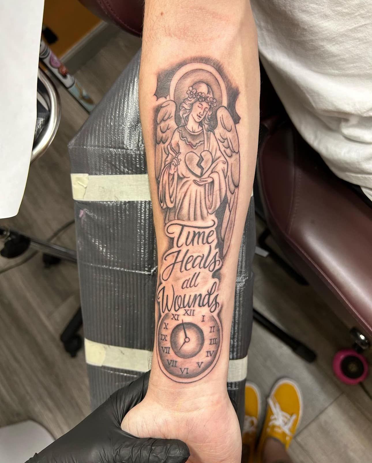 Forearm tattoo of a robed figure with halo and the words “Time Heals All Wounds”